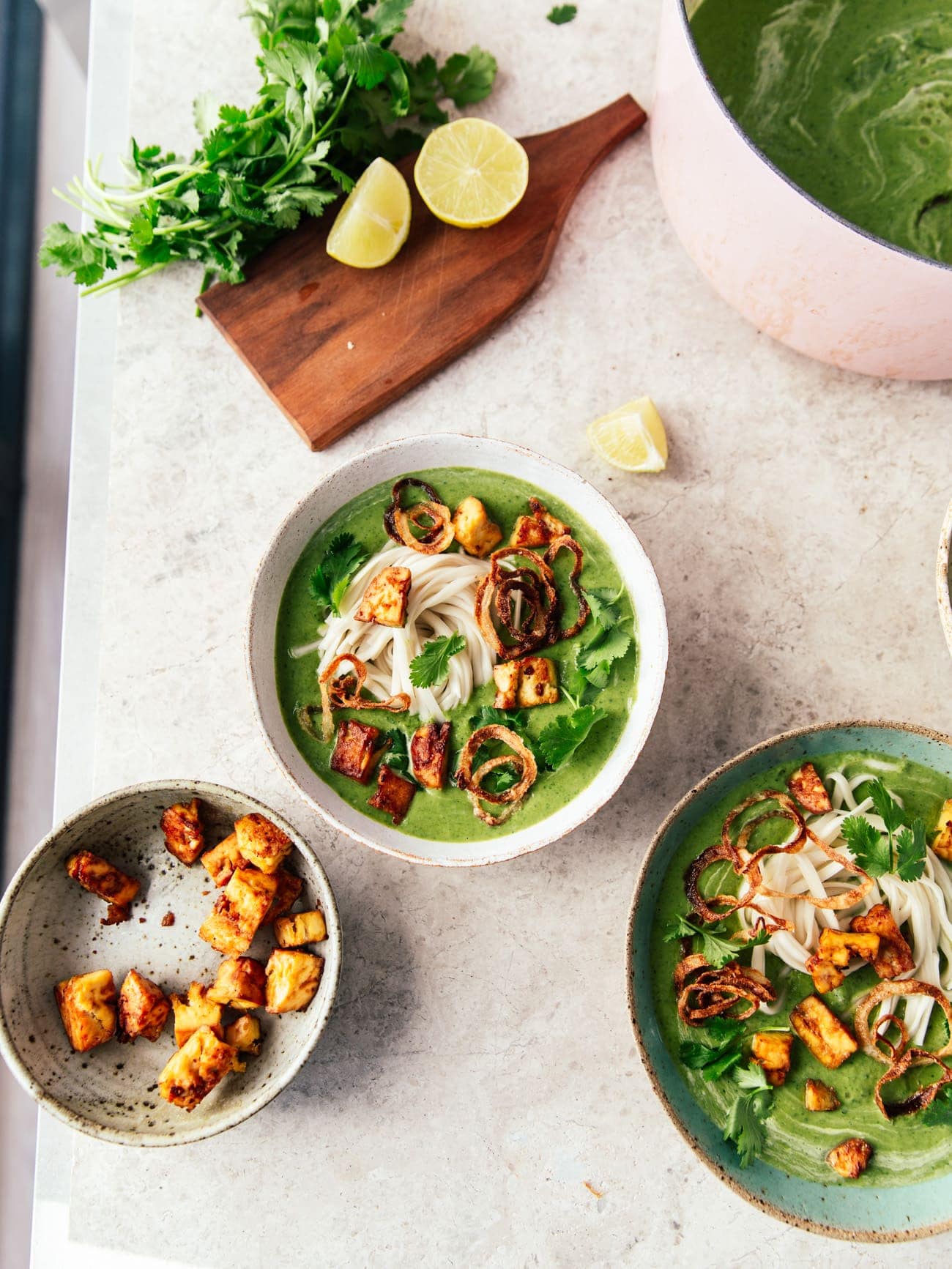 Two bowls and a pot of broccoli soup with smoked tofu, noodles, crispy onions and coriander by Izy Hossack