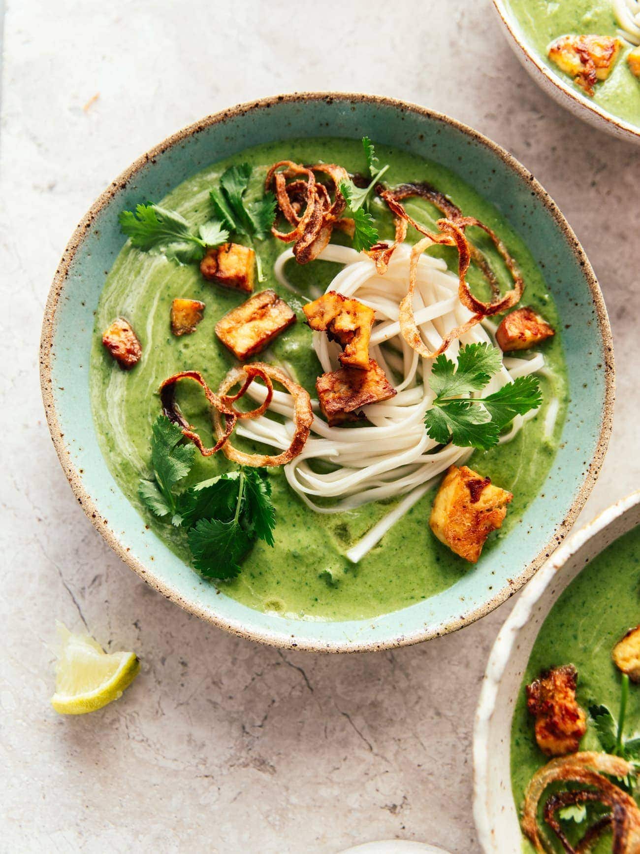 A bowl of creamy broccoli coconut soup with noodles, smoked tofu and crispy onions by Izy Hossack