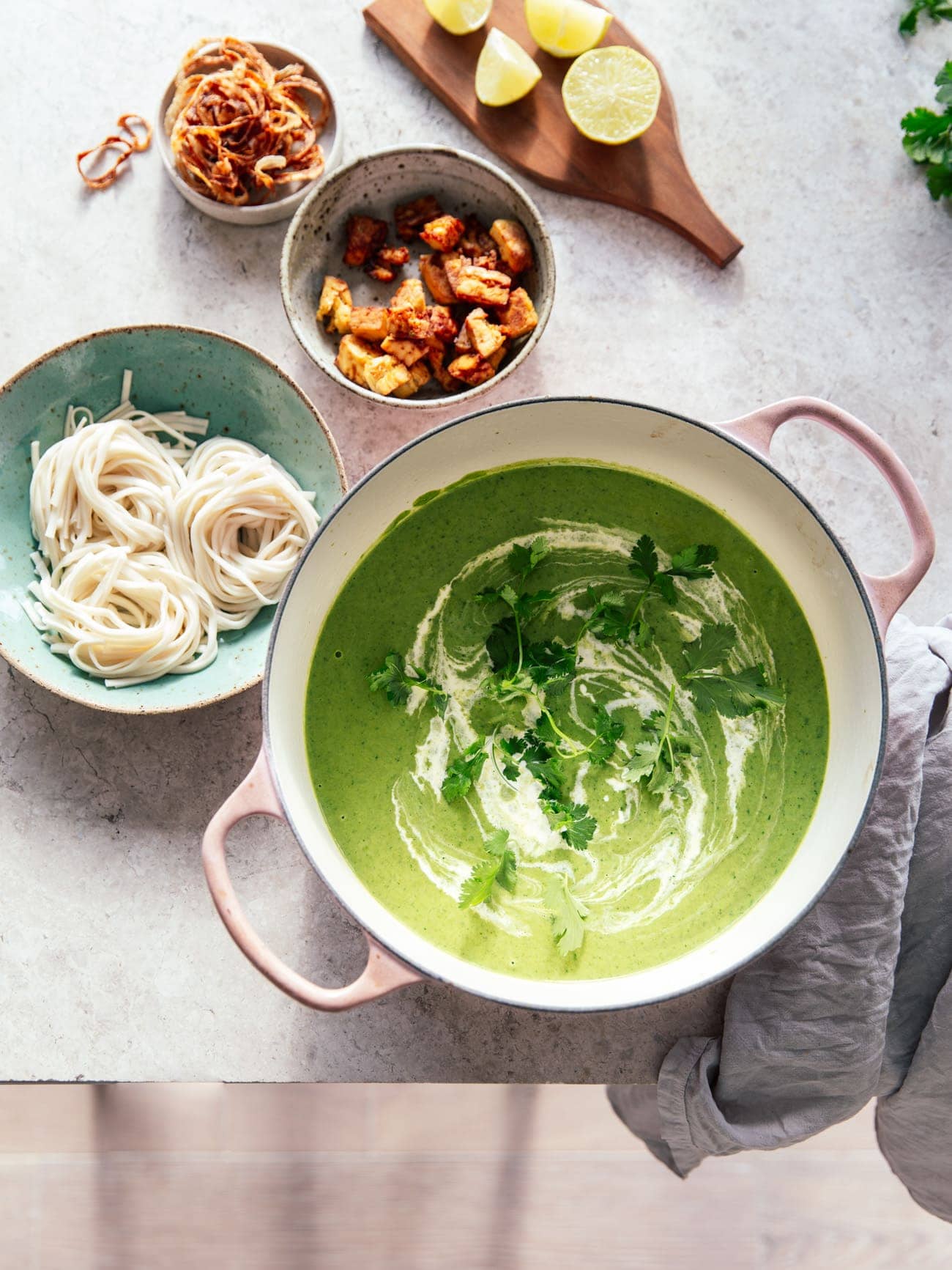 A large pot of creamy broccoli coconut soup served with noodles, smoked tofu and crispy onions by Izy Hossack