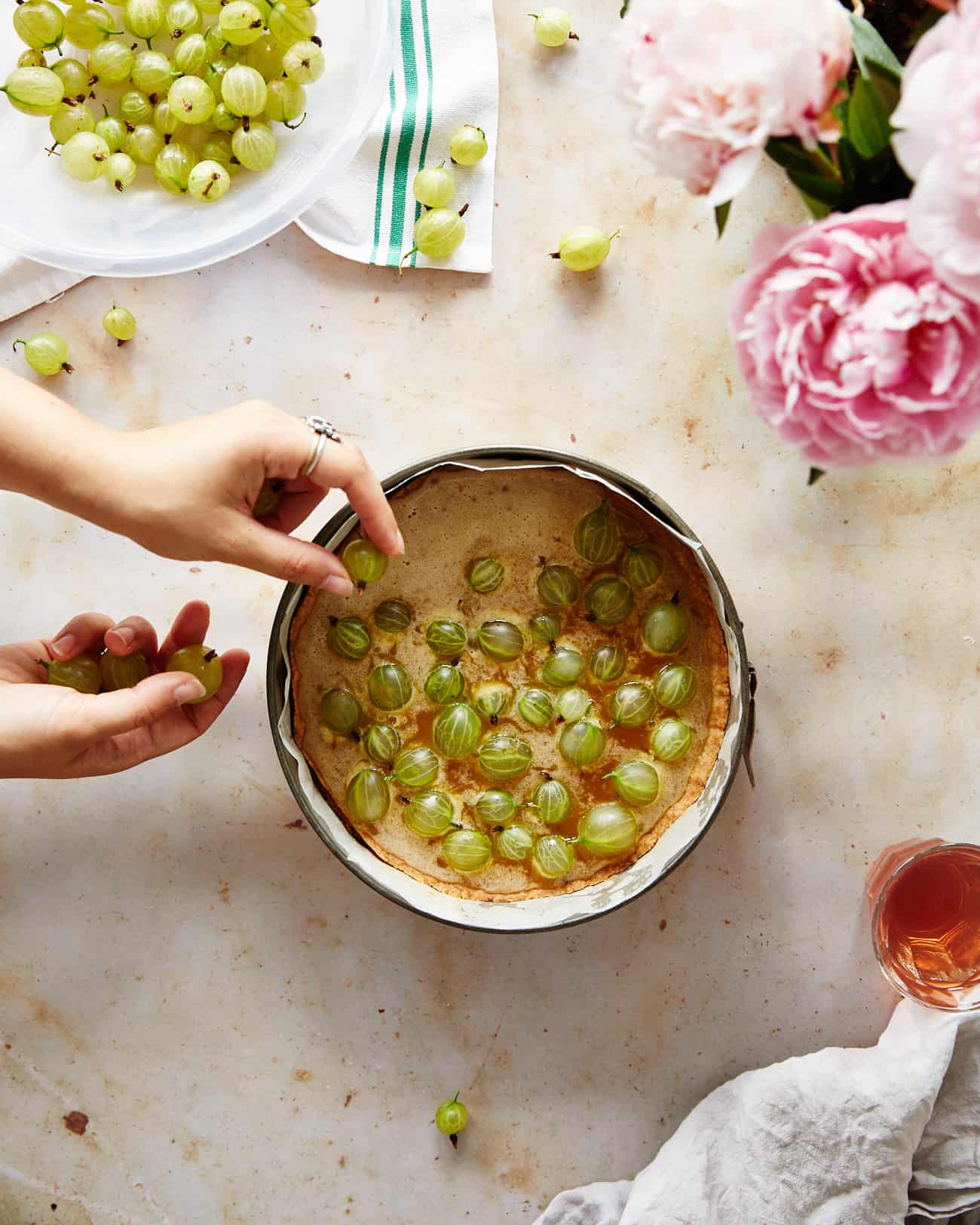 Hands adding gooseberries to an unbaked brown butter tart