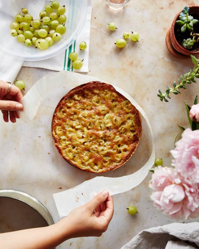 Hands removing baking paper from a brown butter gooseberry tart