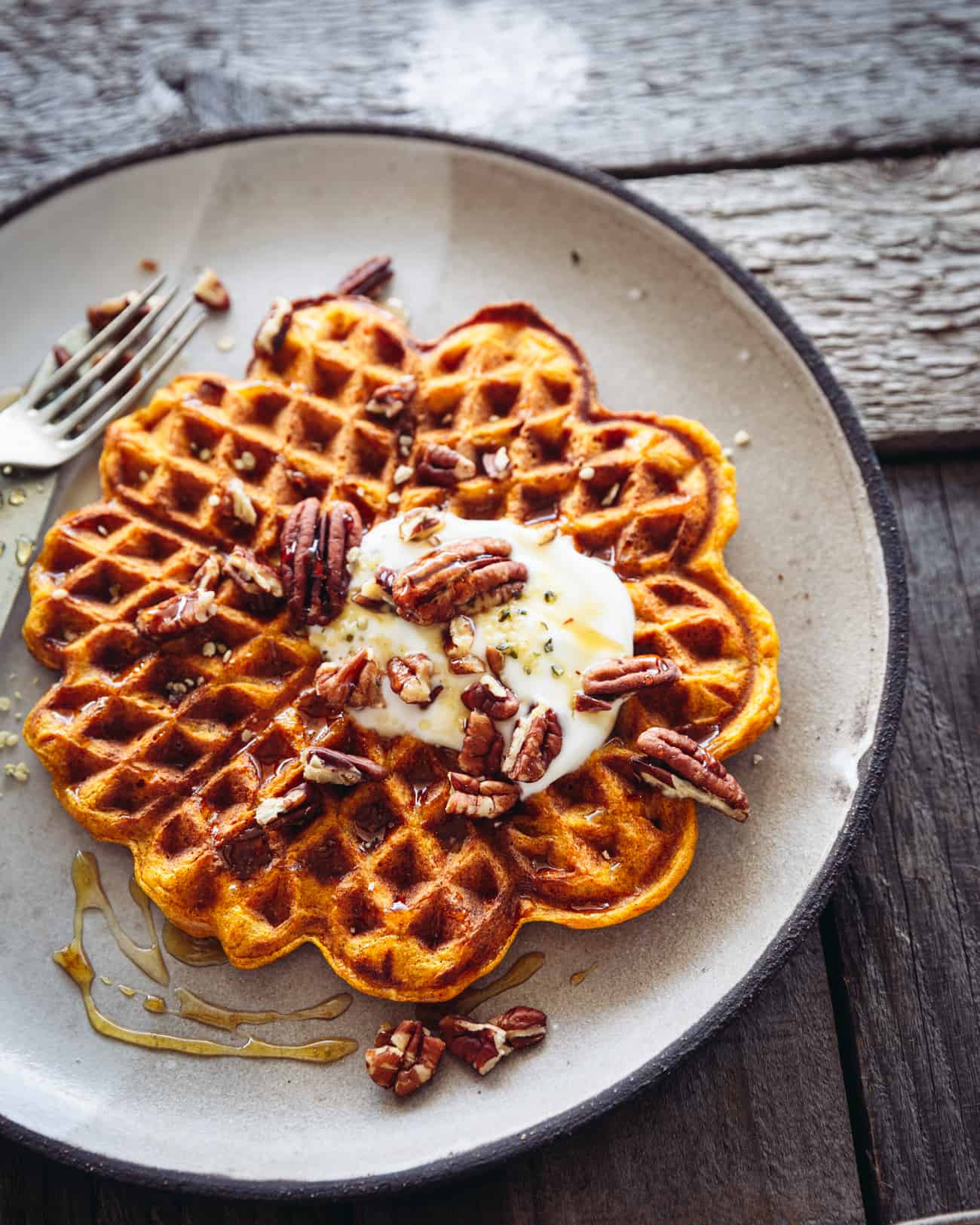a plate with a pumpkin spice waffle and yoghurt and pecans on top