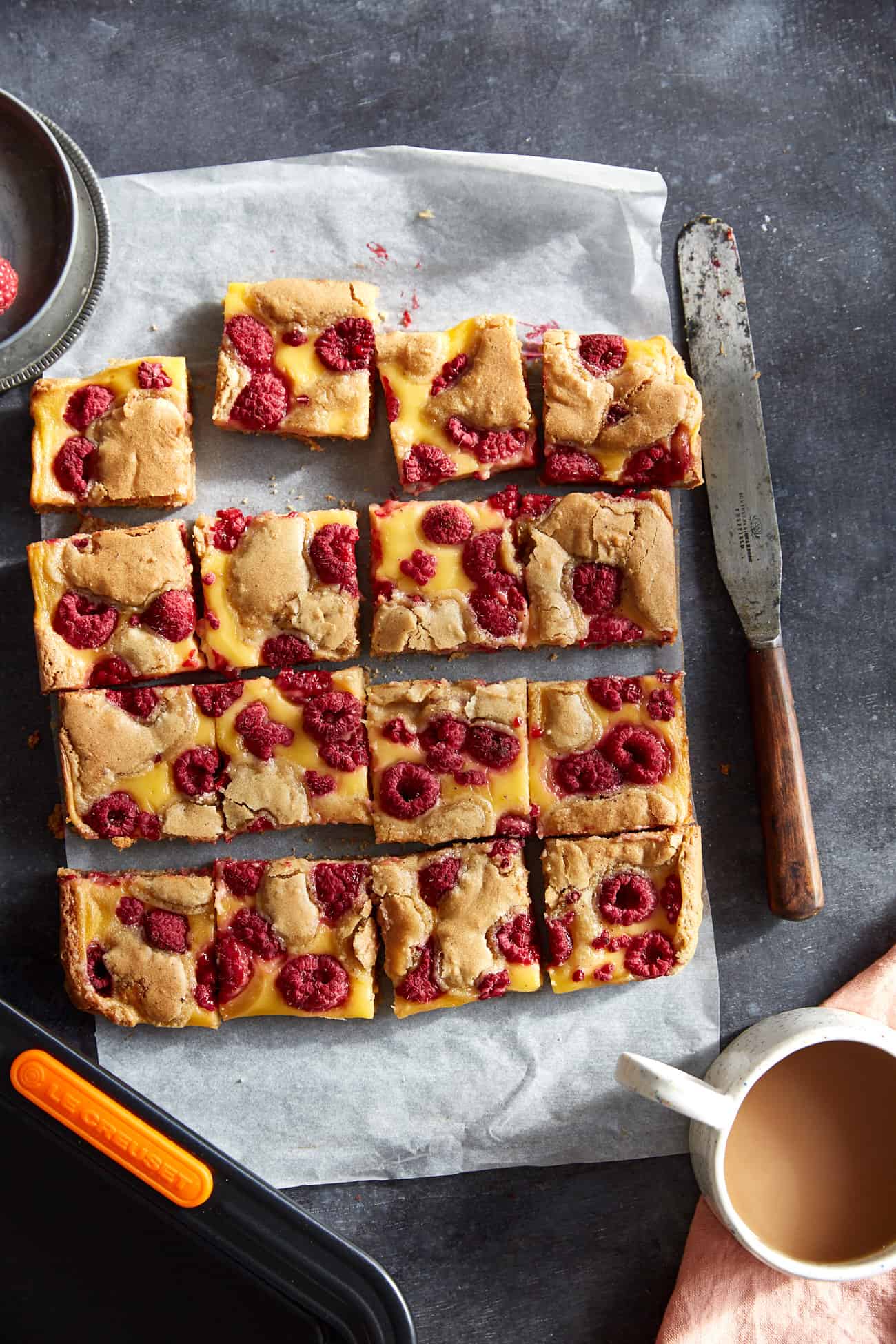 cut raspberry and custard blondies on a dark background with a cup of tea