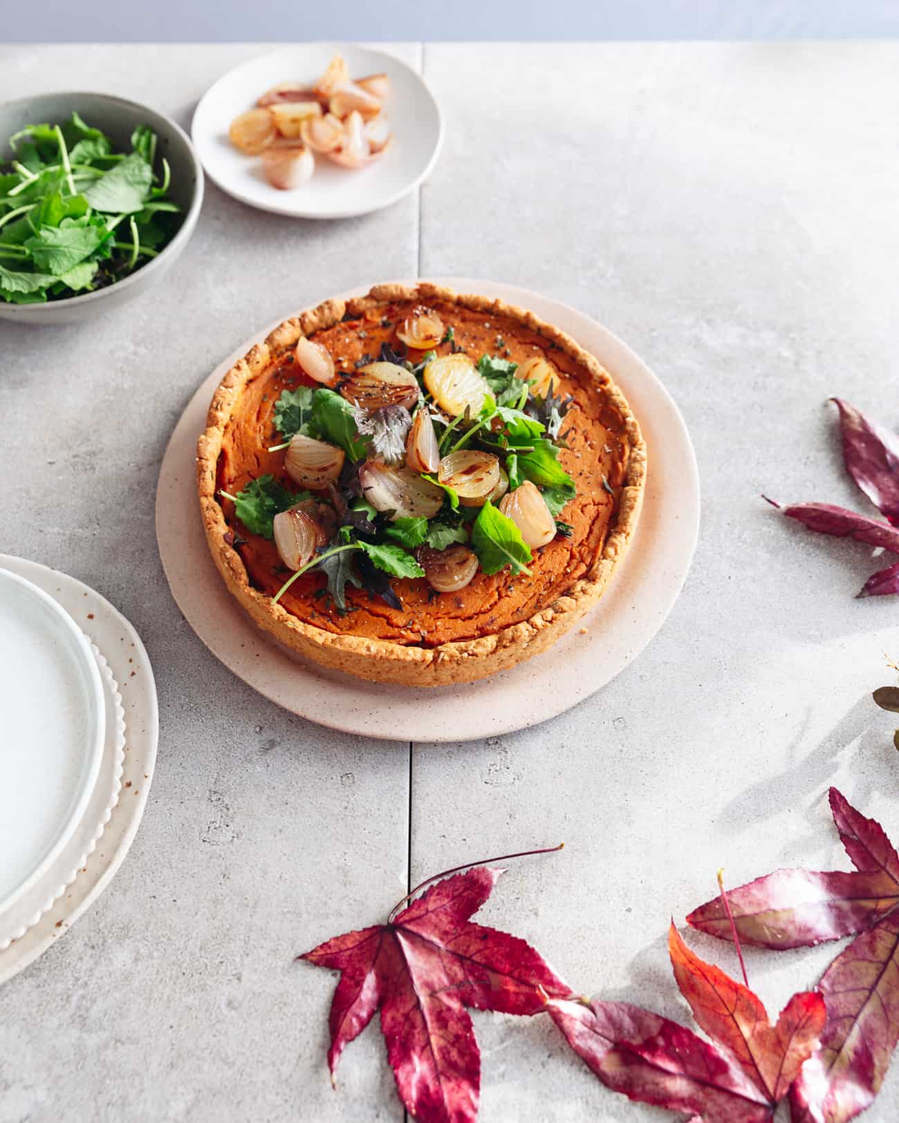 A squash tart with bowls of caramelised shallots and baby kale