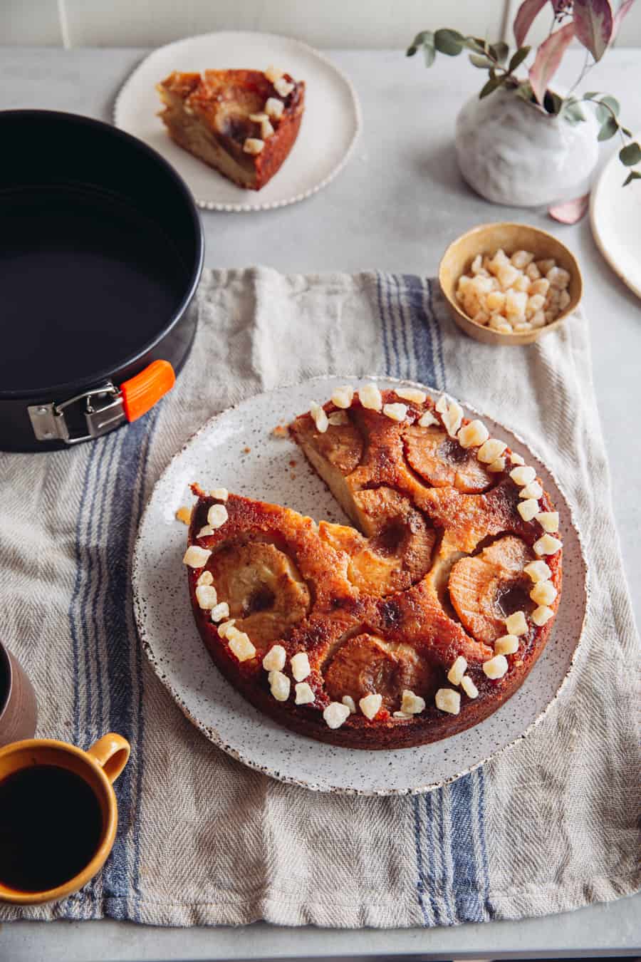 an apple upside down cake topped with crystallised ginger with a slice removed on a striped napkin