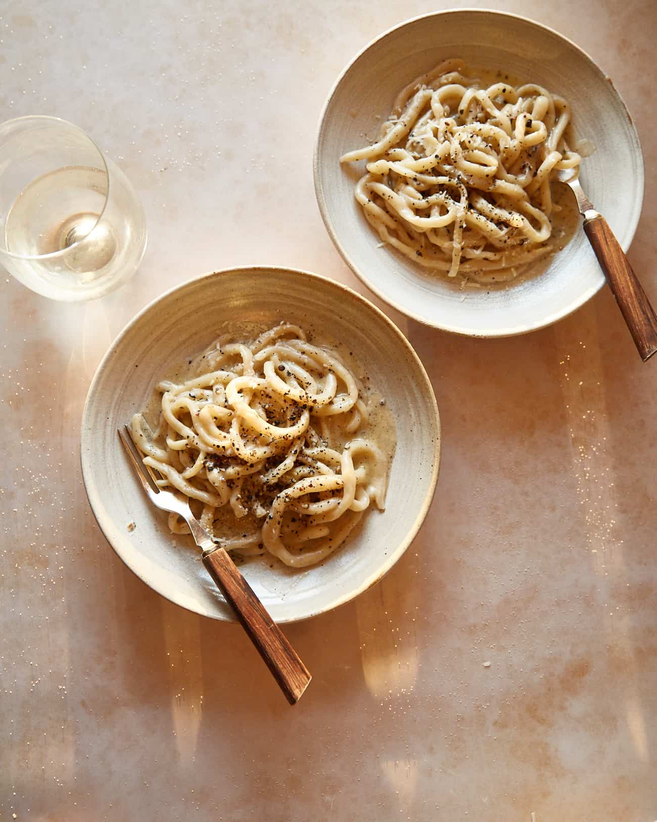 pici cacio e pepe in two bowls with a glass of wine