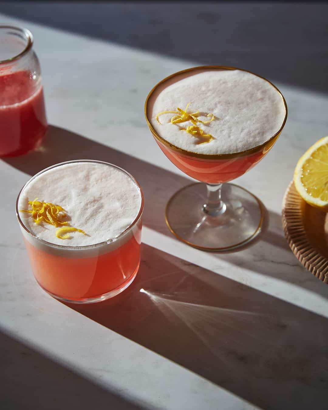 two rhubarb gin sour cocktails with lemon zest on a marble table