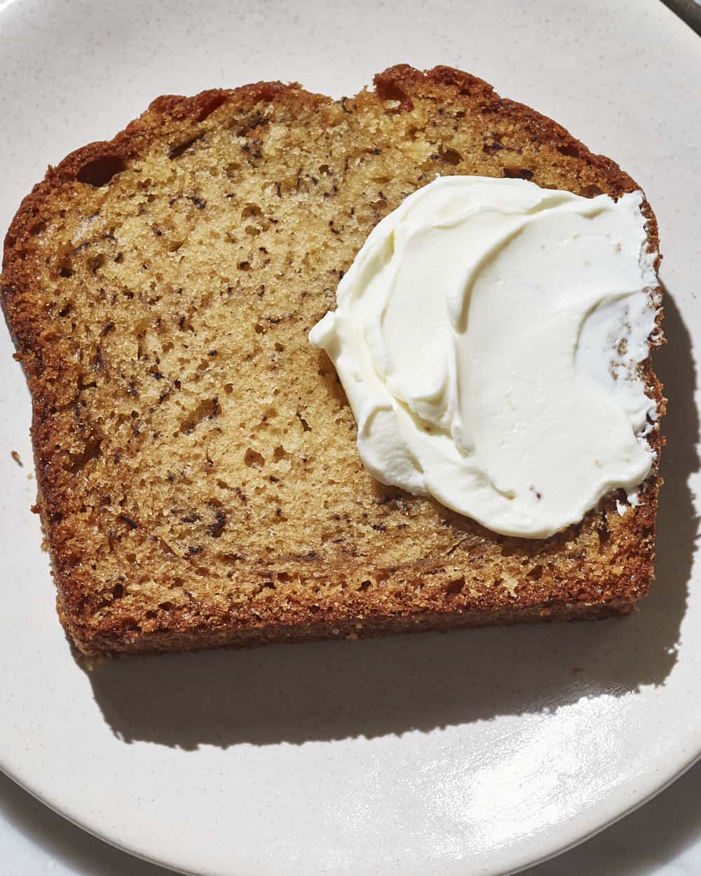 a slice of banana bread on a plate with cream cheese