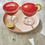 two frozen strawberry daiquiris on a pink plate on a marble table