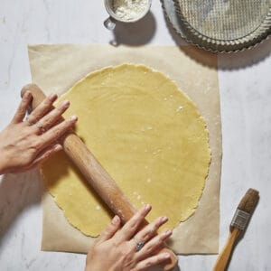 rolling out shortcrust pastry on marble counter with tart tins