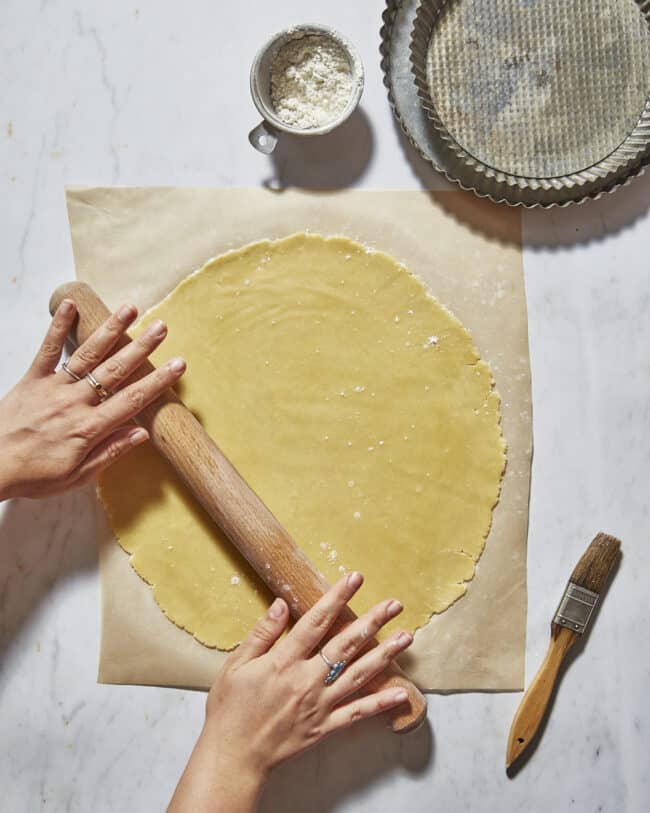 rolling out shortcrust pastry on marble counter with tart tins