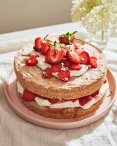 a strawberry sponge cake layered up with whipped cream and fresh berries on a pink plate