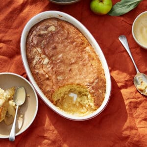 Eve's pudding in an oval dish with a scoop taken, apples in background