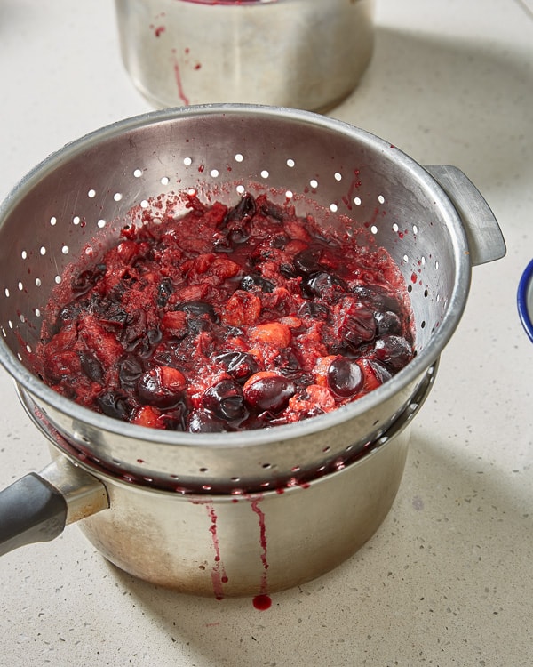 passing cooked damsons through colander set over a pot